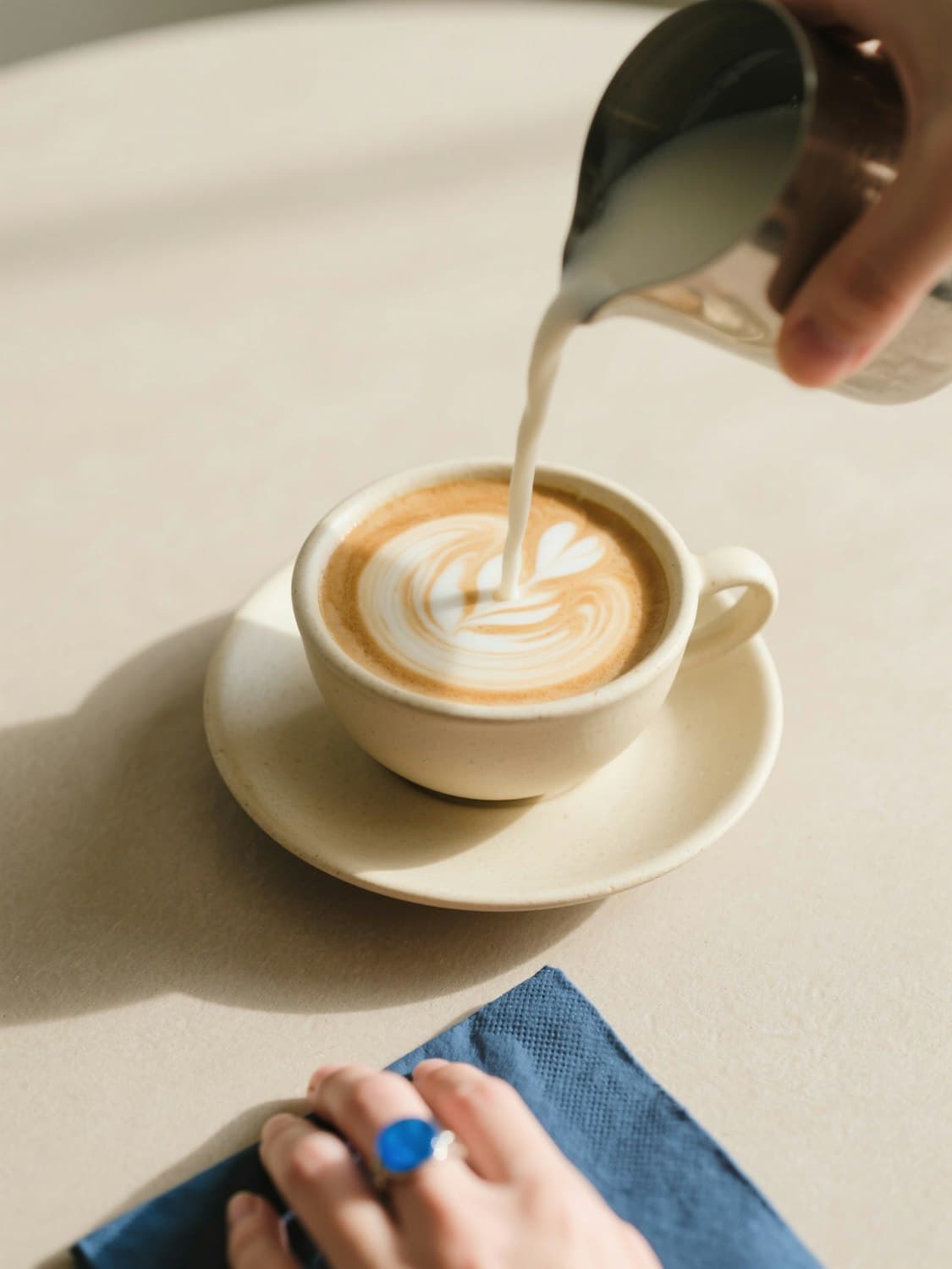 A barista pouring latte art into a ceramic cup